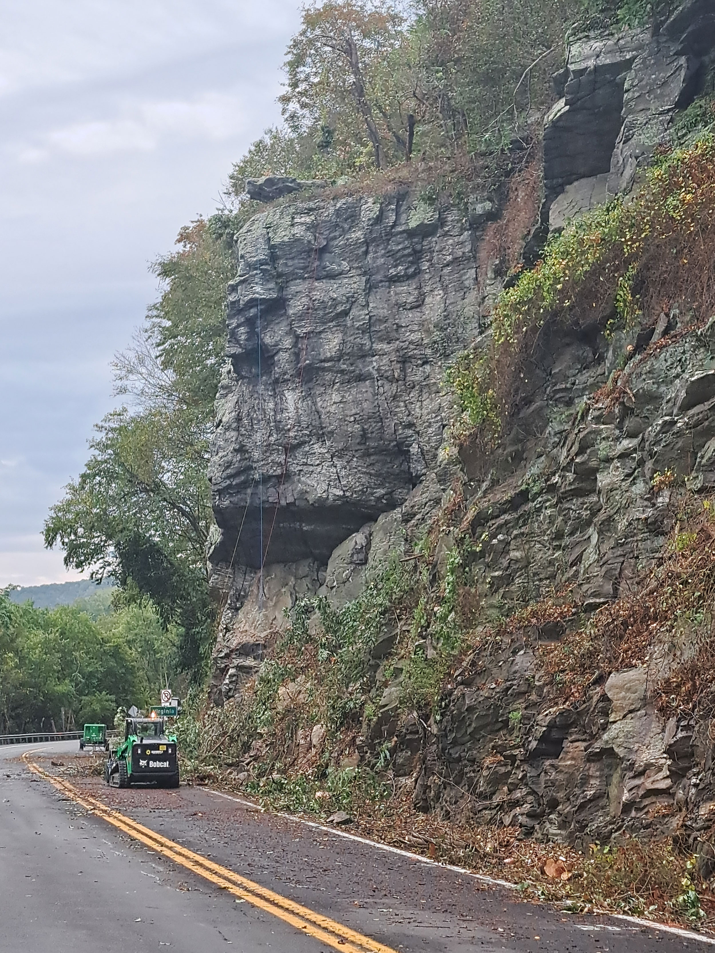 Photo shows the clearing of trees and brush in the vicinity of a large overhanging rock near the WV/VA State Line.  Access ropes are installed to allow for scaling of the rock face.